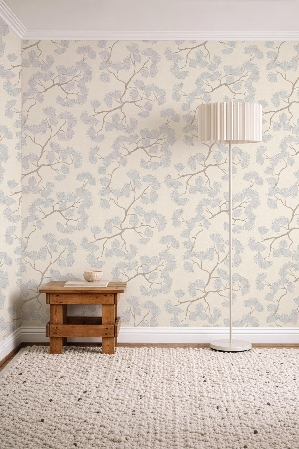 May include: A cozy interior scene featuring a cream-colored rug, a small wooden side table, and a floor lamp. The walls are adorned with wallpaper patterned with light blue and brown branches and leaves, creating a serene atmosphere.