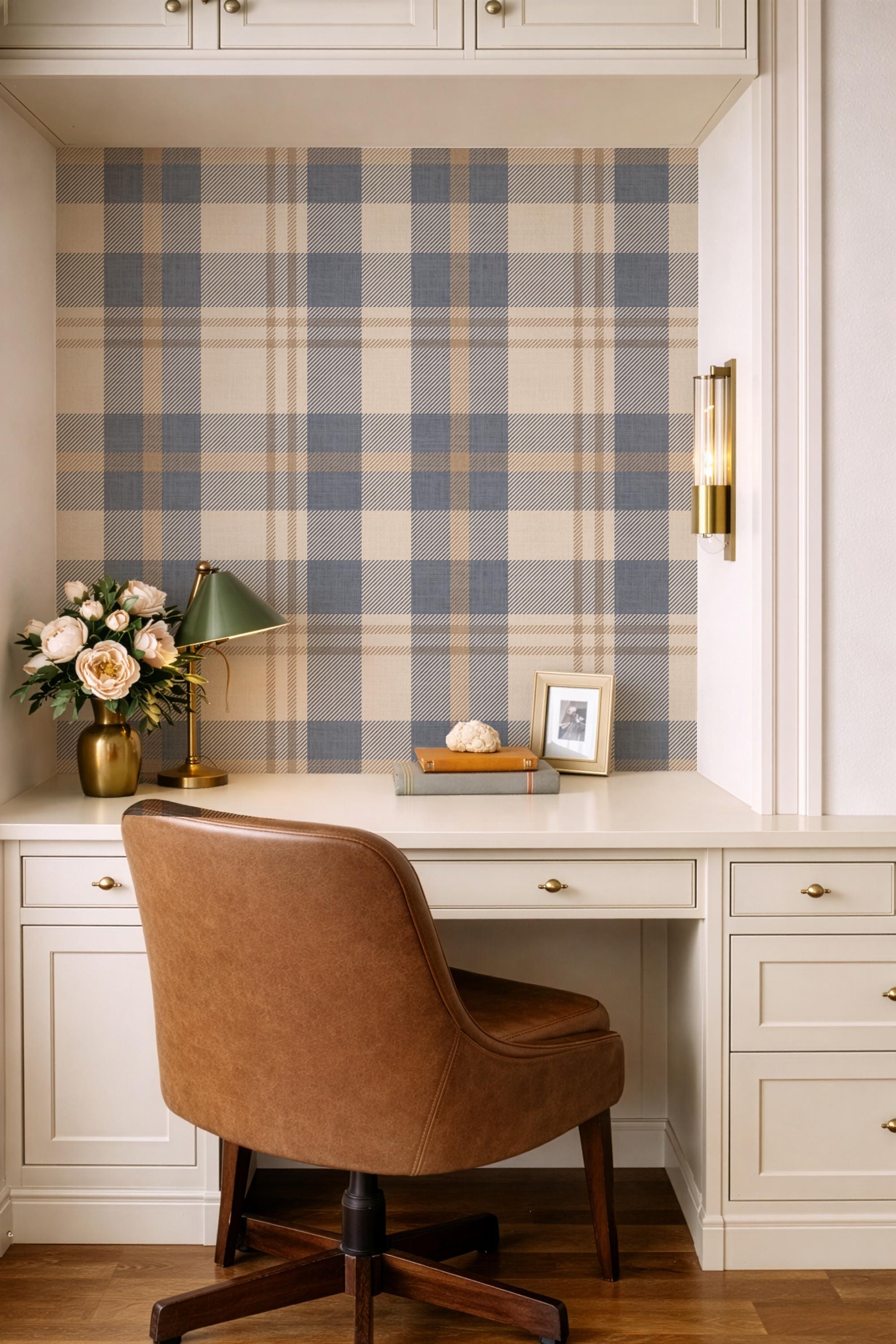 May include: A home office setup featuring a brown leather desk chair, a white desk, and a plaid wallpaper backdrop in shades of blue, beige, and brown. A green desk lamp, a gold vase with flowers, and framed photos add decorative touches.