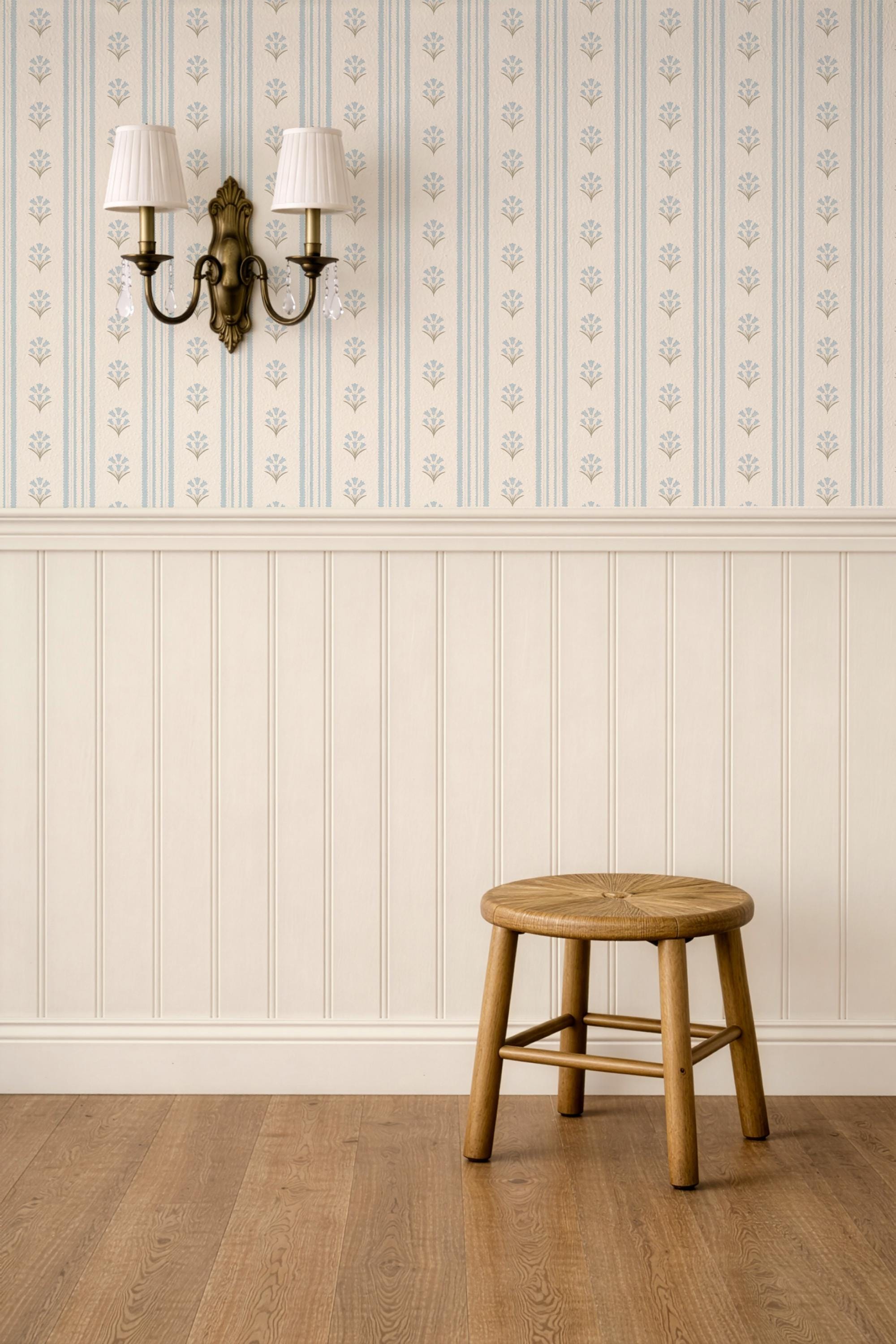 May include: A round wooden stool with a woven seat and four legs connected by a support frame, positioned against a wall with cream-colored wainscoting and wallpaper featuring vertical blue stripes and small floral patterns, with a wall sconce.